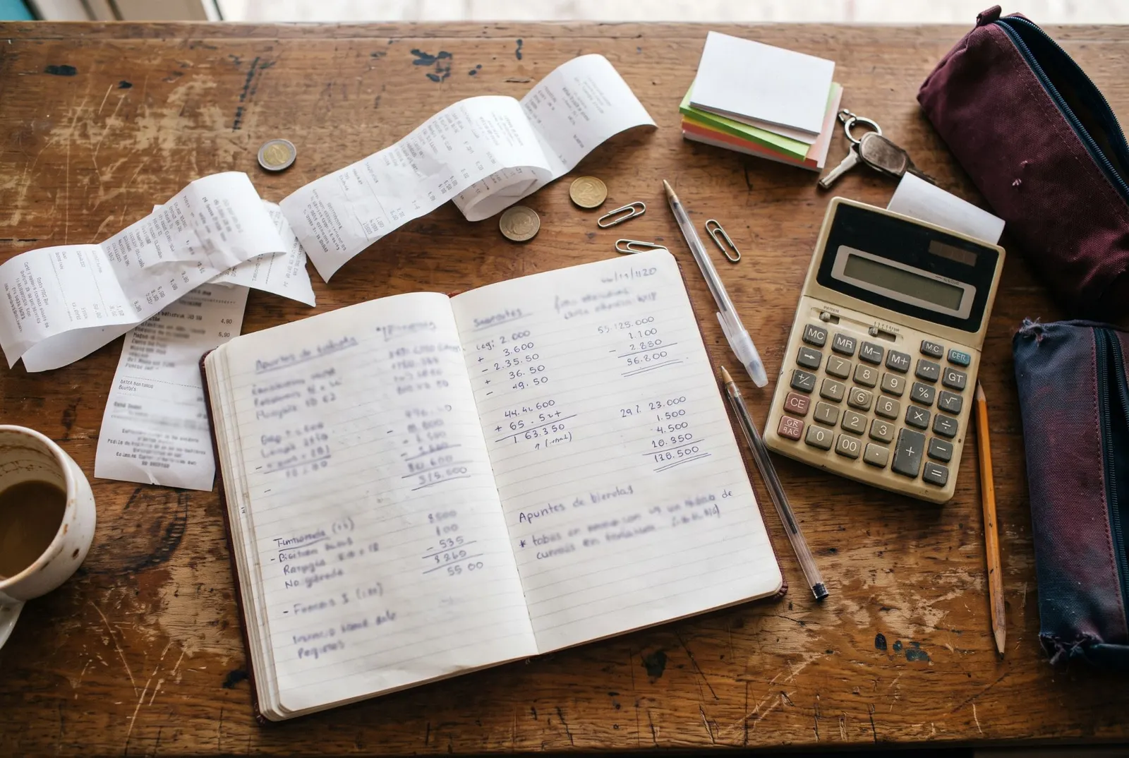 Un cuaderno con cuentas a mano, tickets y una calculadora sobre una mesa de madera.